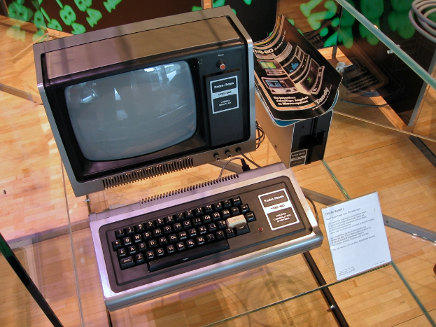 Ein Computersystem auf einem Glastisch mit einer Tafel davor, Broschüren auf dem CPU und einem Holzfußboden im Hintergrund.