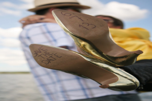 Frauen-High-Heels mit Text darauf, mit einer Person im Hintergrund, die die Beine einer Frau hält.
